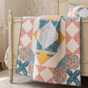 May include: A patchwork quilt featuring a repeating geometric pattern of squares and triangles. The design incorporates floral prints in shades of dusty pink, teal blue, and mustard yellow, interspersed with solid white quilted fabric squares.