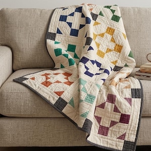 May include: A patchwork quilt featuring a cream-colored base with repeating geometric block patterns in navy blue, mustard yellow, forest green, terracotta orange, and plum purple, finished with a dark gray binding along the edges.