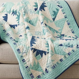 Op de afbeelding: Een doorgestikte sprei met een geometrisch sterpatroon in tinten mintgroen, marineblauw en crème. De stof is voorzien van gedetailleerd stikwerk, met een effen marineblauwe rand en een gestreepte afwerking langs de zijkanten.