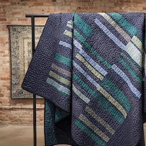 May include: A quilt featuring a dark charcoal gray background with a textured, pebbled surface. It displays a geometric pattern of diagonal stripes in varying shades of teal, sage green, and light blue, arranged in a repeating, staggered layout.