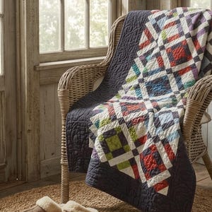 May include: A quilt featuring a patchwork pattern of white, red, green, blue, and purple squares draped over a wicker chair. The quilt has a solid dark grey border with a swirling stitched texture and a white fabric backing visible at the edges.