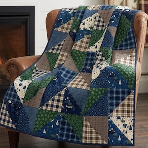 May include: A patchwork quilt featuring a variety of triangular fabric panels in shades of navy blue, forest green, and tan. The design incorporates plaid patterns, solid colors, and prints depicting small pine trees and bear silhouettes.