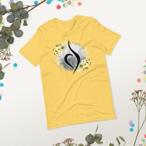 May include: Yellow short-sleeved t-shirt with a black and grey floral design. The design features a stylised symbol with a heart shape and a flower wreath.