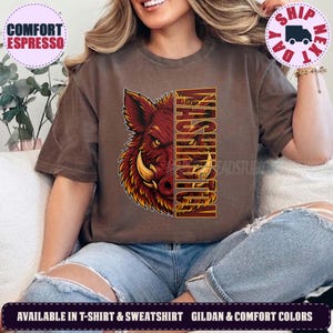 May include: A brown short-sleeved t-shirt featuring a graphic of a wild boar head on the left side and the vertical text WASHINGTON in bold yellow letters on the right side. The boar is rendered in shades of red, orange, and yellow.