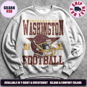 May include: A light grey crewneck sweatshirt featuring a distressed graphic print that reads PROPERTY OF WASHINGTON FOOTBALL 1932. The design includes a large maroon football helmet with a yellow facemask centred over a dark maroon star.