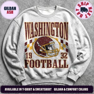 May include: A light gray crewneck sweatshirt featuring a distressed graphic of a maroon football helmet centered between the text WASHINGTON and FOOTBALL, with the numbers 19 and 32 on either side of the helmet and a checkered pattern background.