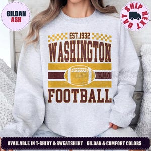 May include: A light gray crewneck sweatshirt featuring a distressed graphic in burgundy and gold. The design includes the text EST. 1932, WASHINGTON, and FOOTBALL, with a central football illustration and a checkered border pattern above the text.