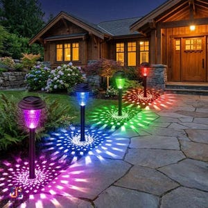 May include: A series of solar-powered garden path lights with black stakes and textured glass tops, emitting vibrant purple, blue, green, and red light patterns onto a stone walkway in front of a wooden house at night.