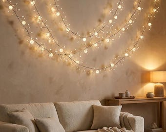 Puede incluir: Una cadena de luces LED de color blanco cálido dispuesta en múltiples bucles sobre una pared. Las luces cuentan con pequeñas bombillas esféricas brillantes unidas a ramas de alambre fino y flexible, creando una iluminación ambiental suave.