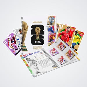 Può includere: Un set di collezione di figurine extra per il mini-album FIFA 2026 con un libro a spirale decorato con un trofeo dorato, accompagnato da diverse figurine di calciatori e una pagina aperta che mostra Luka Modric con la sua firma stampata.