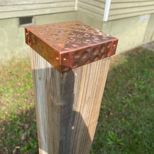 May include: A wooden post with a copper cap. The cap has a hammered texture and is secured with copper rivets.