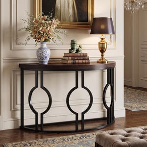 May include: A semi-circular console table with a dark wood top and a black metal frame featuring three circular geometric cutouts. On the table sits a blue and white porcelain vase with flowers, a green stone figurine, and a brass table lamp.