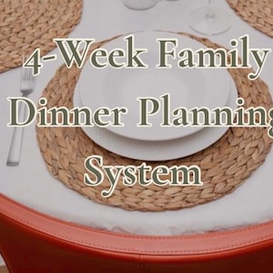 May include: A white dinner plate and bowl set placed on a round woven straw placemat. The text 4-Week Family Dinner Planning System is overlaid on the image. A silver fork and knife are positioned on the white tablecloth near the placemat.