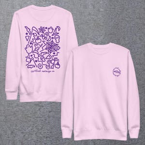 May include: A light pink crewneck sweatshirt featuring a purple graphic print of Halloween icons including ghosts, spiders, webs, bats, and pumpkins on the back, with the text "certified nostalgia co." and a small matching logo on the front.