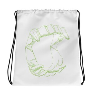 Puede incluir: Una bolsa de cordón blanca con un gráfico de líneas de color verde lima que representa colmillos de vampiro en el centro. El texto Certified Nostalgia Co. está impreso en letras pequeñas de color verde lima cerca de la parte inferior izquierda.