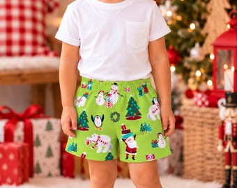 May include: A white short-sleeved t-shirt with a chest pocket paired with bright green shorts featuring a festive holiday print of Santa Claus, polar bears, penguins, snowmen, Christmas trees, and wrapped gift boxes.