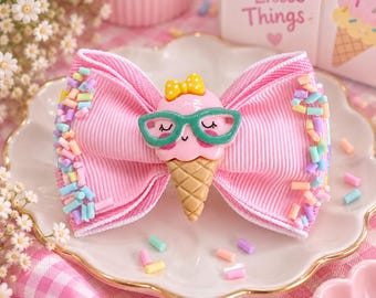 May include: A pink grosgrain ribbon hair bow featuring a central ice cream cone charm with a smiling face, green glasses, and a yellow bow. The ribbon edges are decorated with colorful pastel sprinkles, creating a textured and playful appearance.