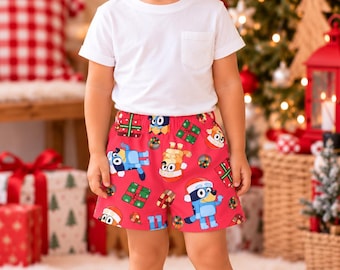 May include: A white short-sleeve t-shirt with a chest pocket paired with red shorts featuring a repeating pattern of Bluey characters wearing Santa hats, wrapped Christmas presents, and colorful holiday ornaments.