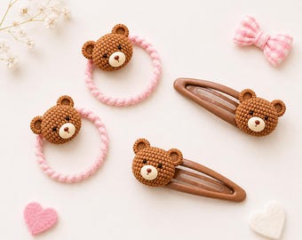 May include: Two pink braided hair ties and two brown metal snap hair clips, each featuring a textured brown bear head with a cream-colored muzzle and black nose. A small pink and white gingham bow and two felt hearts are also included in the set.