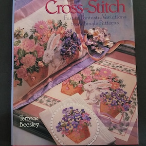 Op de afbeelding: Boekomslag met een kleurrijk kruissteekontwerp met een konijn en bloemen. De titel is "Progressive Cross-Stitch: Fast to Fantastic Variations from Single Patterns" door Terrece Beesley.