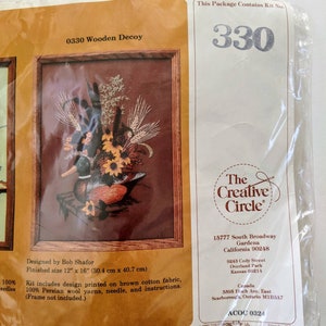 Puede incluir: Un kit de punto de aguja con un señuelo de madera de pato con un arreglo floral marrón, naranja y amarillo. El kit incluye tela de algodón marrón, hilos de lana persa, una aguja e instrucciones. El tamaño terminado es de 30,4 cm por 40,7 cm. El kit es de The Creative Circle.