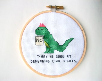 T-Rex is good at defending civil rights, completed cross stitch with T-Rex protesting, in 4 in. natural wood embroidery hoop