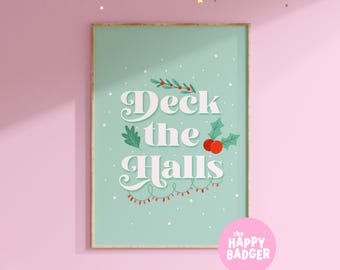 May include: A rectangular wall art print with a light green background featuring the white text Deck the Halls. The design includes illustrations of holly leaves, red berries, and a string of colorful Christmas lights, all set against a snowy backdrop.