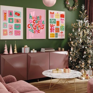 May include: Three framed wall art prints featuring colorful holiday illustrations and the text "having a cosy christmas time" in red and green. The prints are displayed above a dark mauve sideboard with decorative items and a Christmas tree.