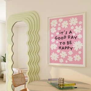Op de afbeelding: Een roze en witte ingelijste print met een wit madeliefjespatroon en de tekst "it's a good day to be happy".