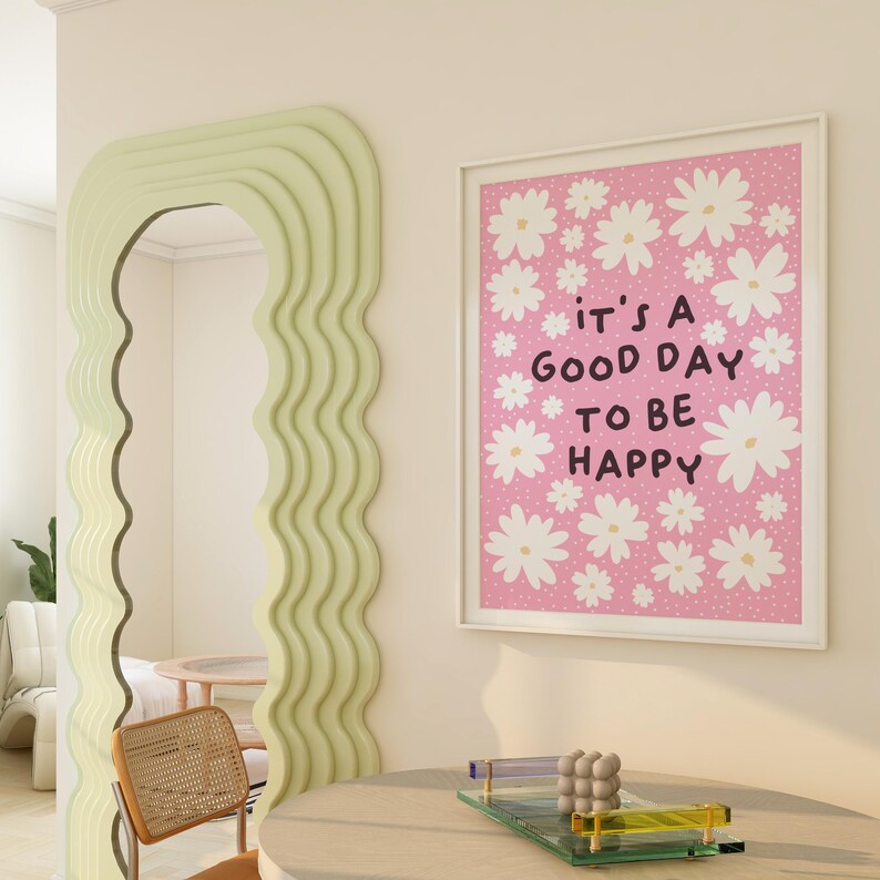 Op de afbeelding: Een roze en witte ingelijste print met een wit madeliefjespatroon en de tekst "it's a good day to be happy".