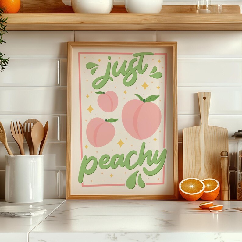 K&ouml;nnte beinhalten: Ein gerahmtes, rechteckiges Wandbild mit cremefarbenem Hintergrund, drei rosa Pfirsichillustrationen und dem gr&uuml;nen Schriftzug "just peachy", umgeben von kleinen gelben Sternakzenten in einem schlichten hellen Holzrahmen.