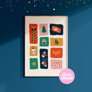 May include: A rectangular wall art print in a light wooden frame featuring a grid of twelve colorful postage stamp-style illustrations of Christmas icons including a gift, tree, house, ornament, mittens, bow, star, and candy cane with a pink logo.
