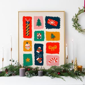 May include: A framed rectangular wall art print featuring a grid of twelve colorful, scalloped-edge rectangular illustrations. The icons include a tall striped gift, a green pine tree, a red present, a house, a Christmas tree, an ornament, mittens, a bow, a star, and a candy cane.