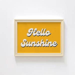 May include: A framed print with a yellow background and white text that reads "Hello Sunshine".