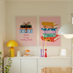 May include: Two pink framed prints with illustrations of stacks of books. The print on the left says "I'll be in my reading nook". The print on the right has the titles of the books: "Guide to Stress-Free Living", "Feminine Bee & Other Recipes", "Hygge", "Wild Mushrooms".