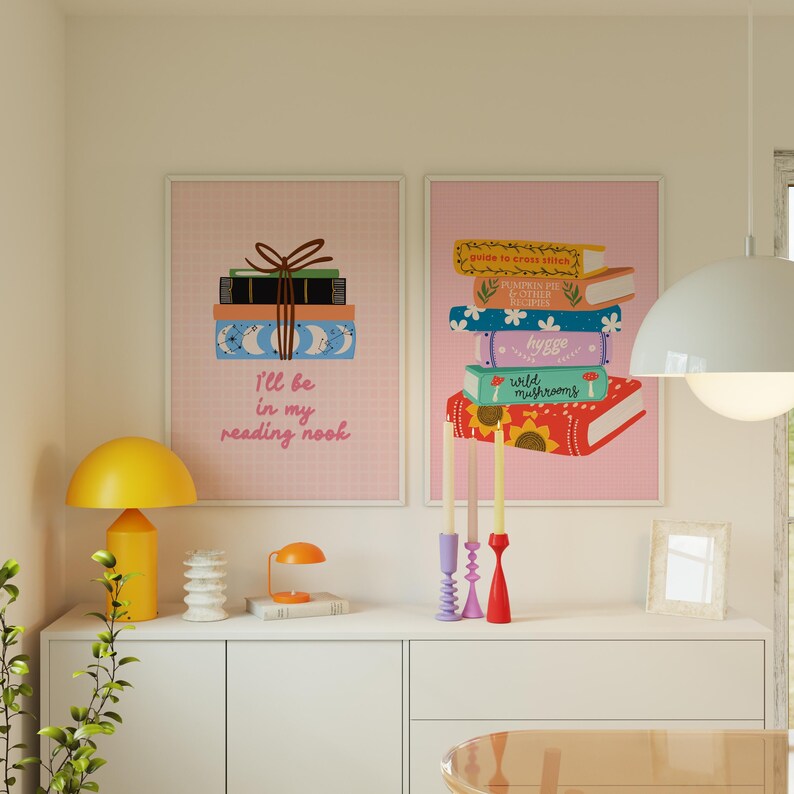 May include: Two pink framed prints with illustrations of stacks of books. The print on the left says "I'll be in my reading nook". The print on the right has the titles of the books: "Guide to Stress-Free Living", "Feminine Bee & Other Recipes", "Hygge", "Wild Mushrooms".