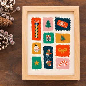 May include: A framed art print featuring a grid of colorful, scalloped-edge rectangles, each containing a holiday-themed illustration including a gift, a pine tree, a house, a gingerbread tree, an ornament, mittens, a bow, a star, and a candy cane.