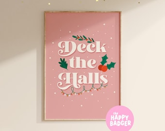 May include: A rectangular wall art print with a dusty pink background featuring the white text Deck the Halls in a retro font. The design includes green holly leaves, red berries, and a string of colorful Christmas lights with white dots.