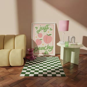 K&ouml;nnte beinhalten: Ein rechteckiger Wandkunstdruck mit cremefarbenem Hintergrund, drei rosa Pfirsichillustrationen und dem gr&uuml;nen kursiven Text "just peachy", der von einem d&uuml;nnen rosa Rand umgeben ist. Das Design enth&auml;lt kleine gelbe Sterne und gr&uuml;ne Blattmotive.