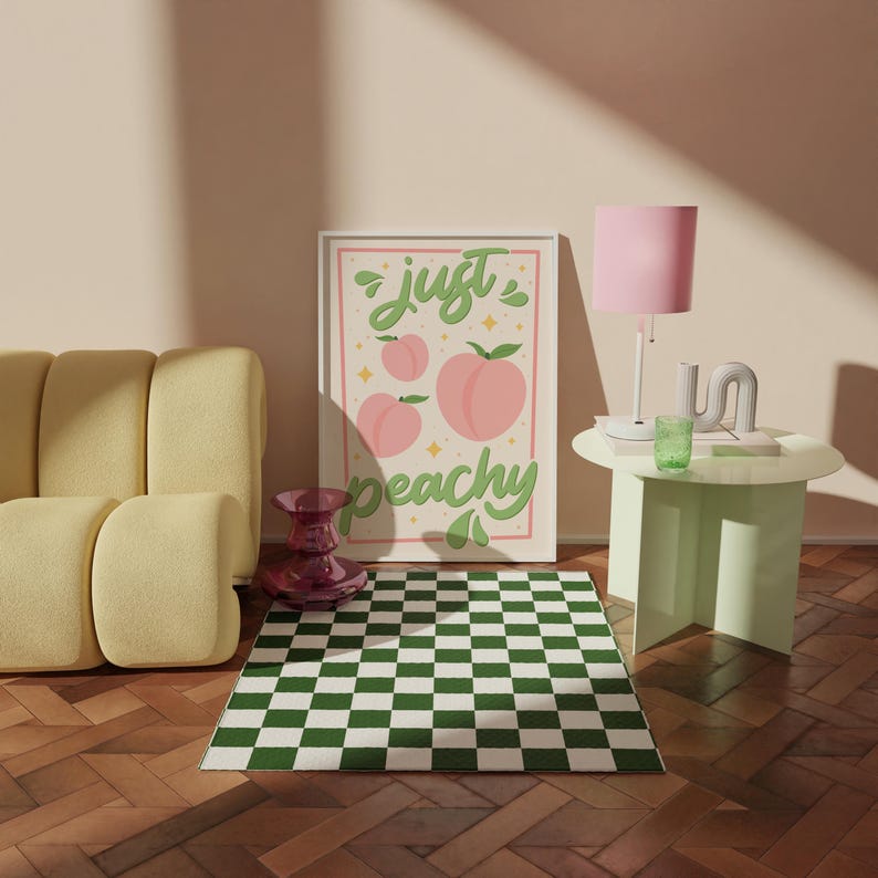 K&ouml;nnte beinhalten: Ein rechteckiger Wandkunstdruck mit cremefarbenem Hintergrund, drei rosa Pfirsichillustrationen und dem gr&uuml;nen kursiven Text "just peachy", der von einem d&uuml;nnen rosa Rand umgeben ist. Das Design enth&auml;lt kleine gelbe Sterne und gr&uuml;ne Blattmotive.