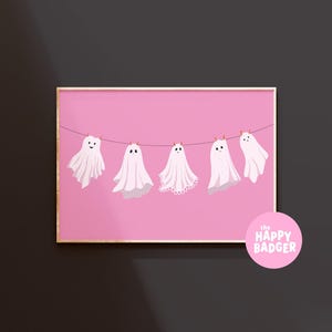 Pode incluir: Uma impress&atilde;o de arte retangular com cinco fantasmas brancos pendurados num estendal contra um fundo rosa s&oacute;lido. Cada fantasma tem um rosto simples e uma bainha &uacute;nica. Um log&oacute;tipo circular rosa apresenta o texto the happy badger em branco.
