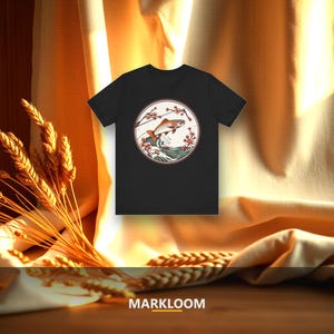 Puede incluir: Una camiseta negra de manga corta con un gráfico circular en el pecho. El diseño muestra un pez saltando sobre olas de color verde azulado estilizadas, enmarcado por ramas delicadas con pequeñas flores rojas. La palabra MARKLOOM aparece impresa abajo.