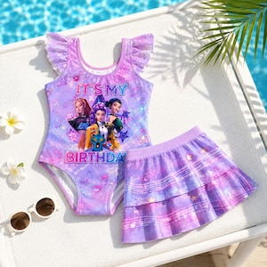 May include: A purple swimsuit with ruffled sleeves and a matching tiered skirt, featuring a graphic of three animated characters and the text IT'S MY BIRTHDAY. The set is decorated with musical notes, stars, and a shimmering galaxy-inspired pattern.