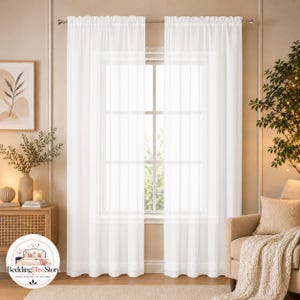 May include: A pair of sheer white curtains hanging from a silver rod over a window. The curtains feature a simple rod pocket header and a lightweight, semi-transparent fabric that allows natural light to filter through into the room.