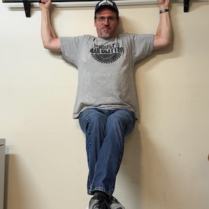 May include: A black metal pull-up bar mounted to a wall with two black brackets. The bar is a straight, cylindrical rod with a textured finish, designed for upper body strength exercises. It is securely attached to the wall at both ends.