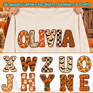 May include: A cream-colored sweatshirt featuring the name OLIVIA in large, patterned letters with Halloween motifs like pumpkins, spiderwebs, bats, and checkers. Below, additional letters display patterns including ghosts, candy corn, and floral designs.