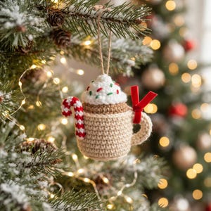 Può includere: Una decorazione natalizia all'uncinetto a forma di tazza beige riempita di panna montata bianca e zuccherini colorati. Un bastoncino di zucchero a righe rosse e bianche è attaccato al lato e un piccolo nastro di velluto rosso è legato al manico.