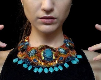 May include: A woman wearing a black top with a colorful beaded necklace. The necklace features turquoise, orange, and gold beads.