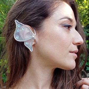 以下が含まれることがあります： 青いアクセントが付いた銀色の蝶の耳飾り。耳飾りは左耳につけられています。