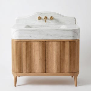 Luxury Carrara marble bathroom vanity featuring a handcrafted integrated stone sink with a softly curved backsplash, genuine white marble with elegant gray veining, brushed brass wall-mounted faucet, and a fluted natural oak cabinet. This custom marble vanity combines timeless European craftsmanship with warm natural wood, creating a sophisticated focal point for luxury bathrooms, powder rooms, and designer interiors.